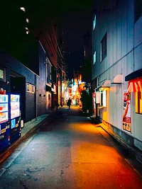 Man Walking Down a Dark Backstreet, Tokyo, JapanA lone man walks down a dark back alley lined with drink vending machines and signs for restaurants and bars in Taito City, Tokyo, Japan.