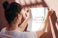 Woman attaching a white poster mockup to a pastel pink wall