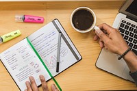 Person's hands on notebook and a cup of coffee.