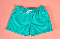 Teal men's swim shorts on a pink background.