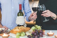 Couple toasting glasses of red wine with snacks set out on table.