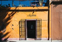 Exterior of a small yellow building with a bar inside. The name of the establishment above the door tells us it's a Mexican bar.