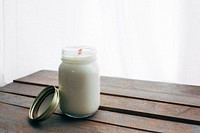 One tall homemade white jar candle on wooden table.