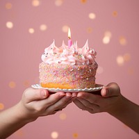 Hand holding birthday cake in studio pink pastel background. 