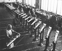 A row of seventy-five millimeter pack howitzers being assembled in the Erie, Pennsylvania, General Electric plant while inspectors watch. A total of twenty-three are shown. These howitzers are being produced largely on machinery formerly used for making streetcar motors. Sourced from the Library of Congress.