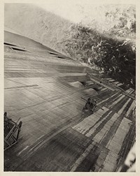 Grand Coulee Dam, Columbia Basin Reclamation Project, Wash. Looking down the face of the dam from the roadway on top. Men are riding a skip to the area to be repaired. Sourced from the Library of Congress.