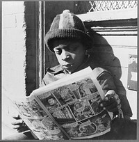 Washington, D.C.  youth reading a funny paper on a door step in the Southwest section. Sourced from the Library of Congress.