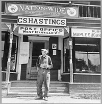 West Danville, Vermont. Frank Goss, seventy-one year old farmer, in front of Gilbert S. Hastings's general store and post office reading his mail, which includes a postcard saying that his last year's hired man "won't be around for haying this year on account of he's in Californi' in the Navy". Sourced from the Library of Congress.