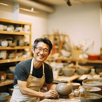 Photo of a thin middle age asian man wearingglasses, casual clothes and apron making pottery. 