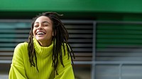 a woman with dreadlocks smiling wearing lime green sweater, playful poses, close up, outdoor city, cool.  