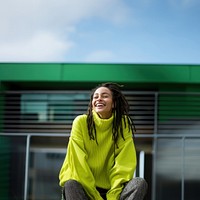 a woman with dreadlocks smiling wearing lime green sweater, playful poses, close up, outdoor city, cool. AI generated Image by rawpixel. 