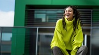 a woman with dreadlocks smiling wearing lime green sweater, playful poses, close up, outdoor city, cool.  