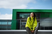 a woman with dreadlocks smiling wearing lime green sweater, playful poses, close up, outdoor city, cool.  