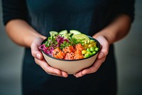 A moman holding poke bowl food salad midsection. 