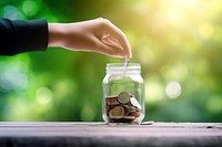 Photo of hand putting Coins in glass jar for giving and donation concept.  