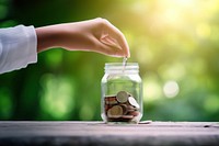 Photo of hand putting Coins in glass jar for giving and donation concept.  