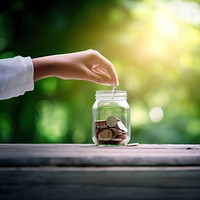 Photo of hand putting Coins in glass jar for giving and donation concept.  