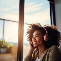 photo of A black woman sitting on a couch happy with wearing headphones in a minimal living room. 