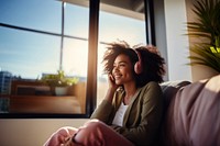 photo of A black woman sitting on a couch happy with wearing headphones in a minimal living room. 