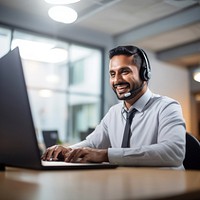 Photo of indian man working at call center, smilling talking to a laptop. 