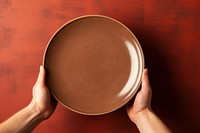 Hands holding a plain plate brown bowl hand. 