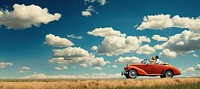 Photo of couple driving in red vintage car on countryside. 