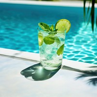 a photo of a mojito cocktail laying near a cool blue pool.  