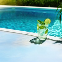 a photo of a mojito cocktail laying near a cool blue pool.  