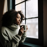 Photo of Thoughtful black woman with coffee cup looking through window in winter season.  