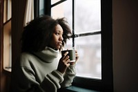 Photo of Thoughtful black woman with coffee cup looking through window in winter season.  