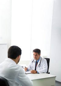 Photo of doctor is talking with patient and making notes while sitting in hospital.  