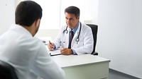 Photo of doctor is talking with patient and making notes while sitting in hospital.  