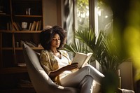 Photo of an african women wearing casual clothes reading book on an armchair, modern livingroom.  