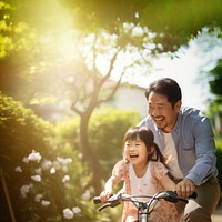 photo of an Asian father helps young daughter ride a bicycle.  