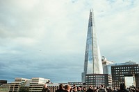 A small crowd of people at the bottom of the image gives perspective on the huge, "Shard" skyscraper in London, England. It towers above all other buildings like a modern, glass steeple.