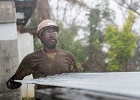 U.S. Navy Construction Electrician Constructionman Akeem Braddy, from Eastman, Georgia, assigned to Navy Mobile Construction Battalion (NMCB) 1, detachment Guam, grabs a metal roofing sheet from a flatbed truck before reconstructing a roof for a home affected by Typhoon Mangkhut in the Commonwealth of the Northern Mariana Islands, October 21, 2018.