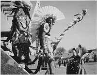 Three Indians in headdress in foreground watching tourists, "Dance, San Ildefonso Pueblo, New Mexico, 1942." Photographer: Adams, Ansel, 1902-1984. Original public domain image from Flickr