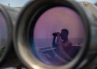 U.S. Navy Culinary Specialist 2nd Class Adrian Bradford uses binoculars to scan the ocean during a bridge watch aboard the guided-missile destroyer USS Bainbridge (DDG 96) in the Arabian Gulf, August 3, 2019.