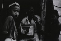 A village elder shows little boys a photo of King Taufa getting his smallpox inoculation. Original public domain image from Flickr