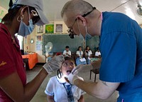 U.S. Navy Cmdr. Bradley J. Smith, right, a dentist, examines a patient before extracting a tooth during a dental and civic action project at San Miguel National High School in San Miguel, Philippines.