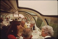 Passenger service representative for Amtrak discusses the train system with travelers in the observation car of the Empire Builder enroute from Chicago to East Glacier Park, Montana, and Seattle, Washington, June 1974. Photographer: O'Rear, Charles. Original public domain image from Flickr