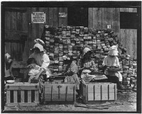 A mother hulling berries while she nurses her infant. Her other children sit beside her, also at work. Little Mabel Guthrie, 4 years old, started working last year, May 1910. Photographer: Hine, Lewis. Original public domain image from Flickr