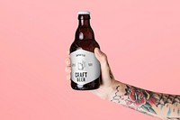 Tattooed arm holding a brown glass bottle psd mockup