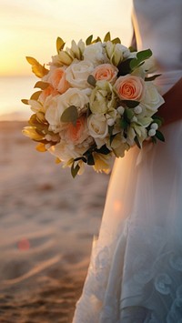 Closeup groom and bride have bouquet at the sunset beach, focus on bouquet.  