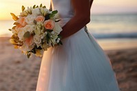 Closeup groom and bride have bouquet at the sunset beach, focus on bouquet.  