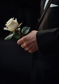 photo of hand in suit put white rose on a funeral casker.  