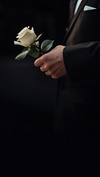 photo of hand in suit put white rose on a funeral casker.  