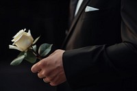 photo of hand in suit put white rose on a funeral casker.  