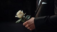 photo of hand in suit put white rose on a funeral casker.  