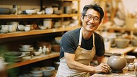 Photo of a thin middle age asian man wearingglasses, casual clothes and apron making pottery. 